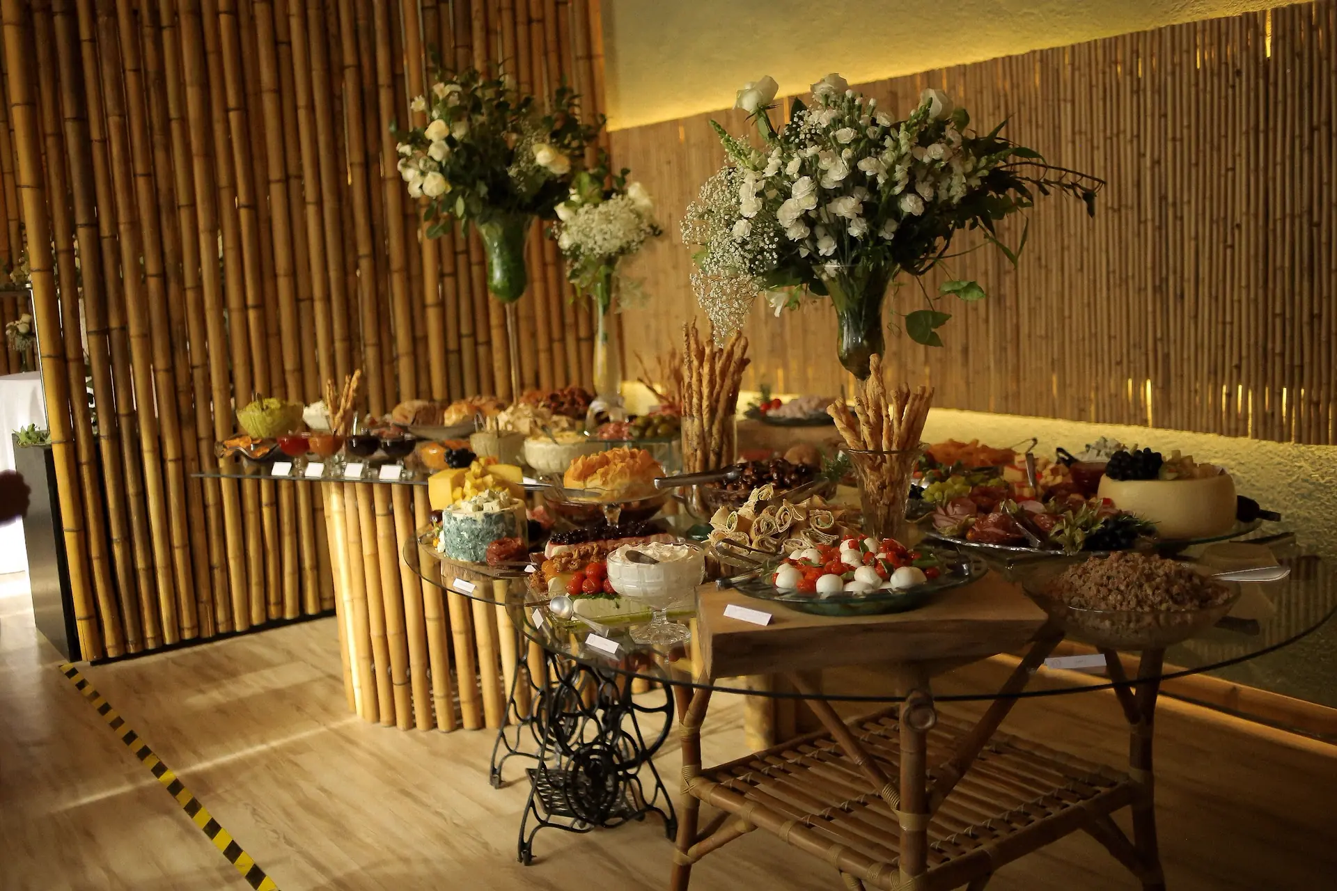 Mesa de antepastos completa com frios, queijos e arranjos florais