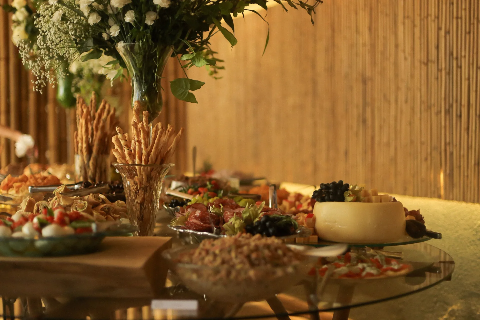 Buffet de aperitivos com arranjo floral alto e parede de bambu