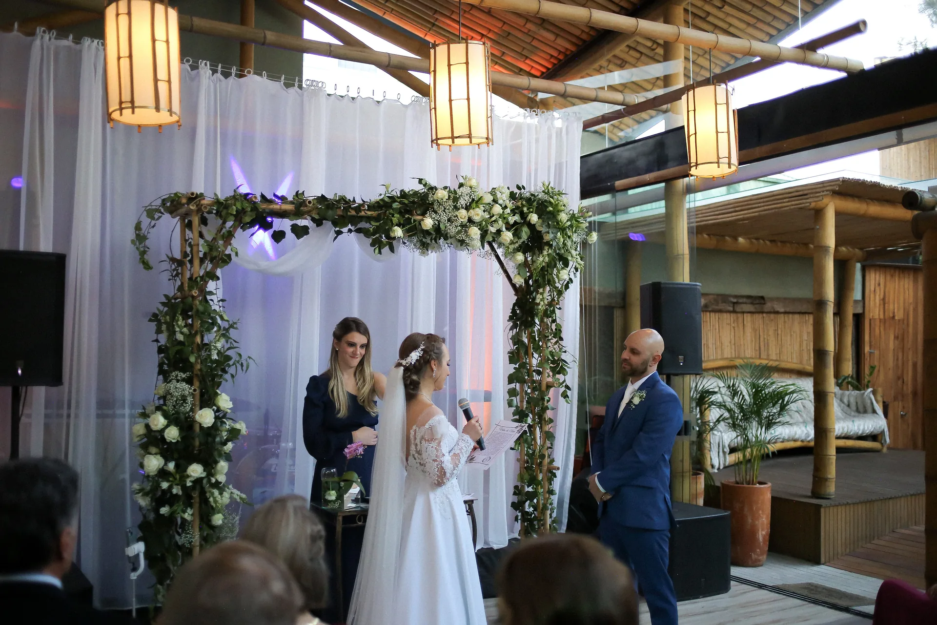 Altar de casamento com cortinas brancas e arco de flores sob o teto de bambu