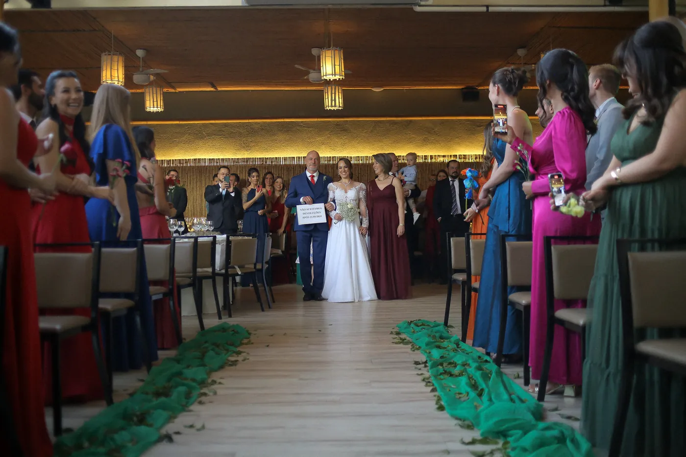Entrada da noiva pelo corredor com convidados de pé no salão de bambu iluminado