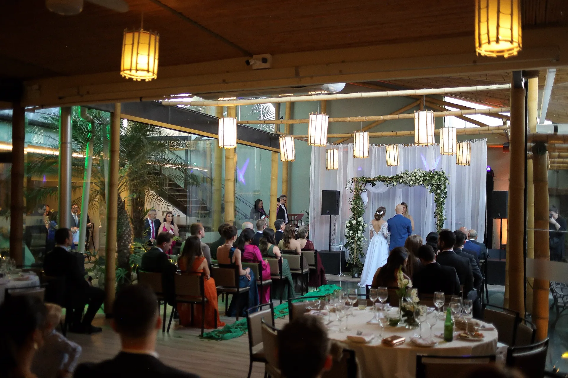 Vista ampla do salão de eventos com mesas postas, convidados e altar ao fundo