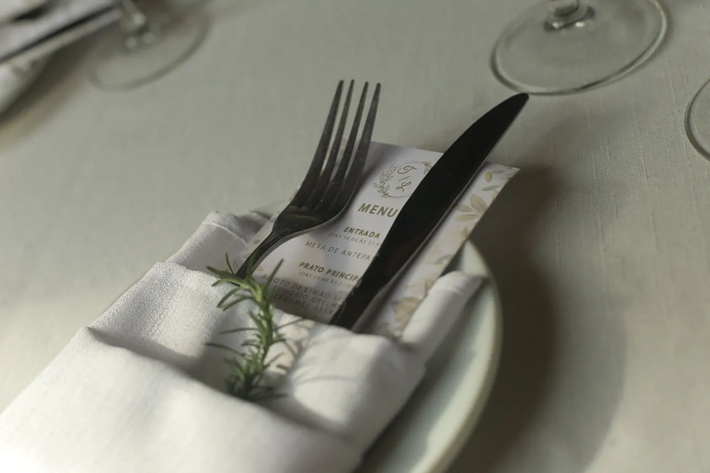 Menu impresso sobre guardanapo com talheres e ramo de alecrim no lugar posto