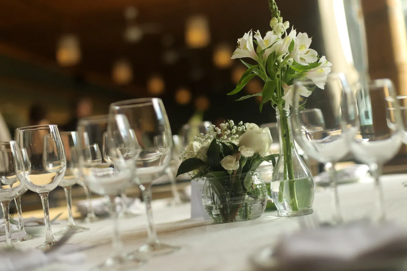 Detalhe de taças de cristal e arranjo de flores brancas com luzes quentes desfocadas