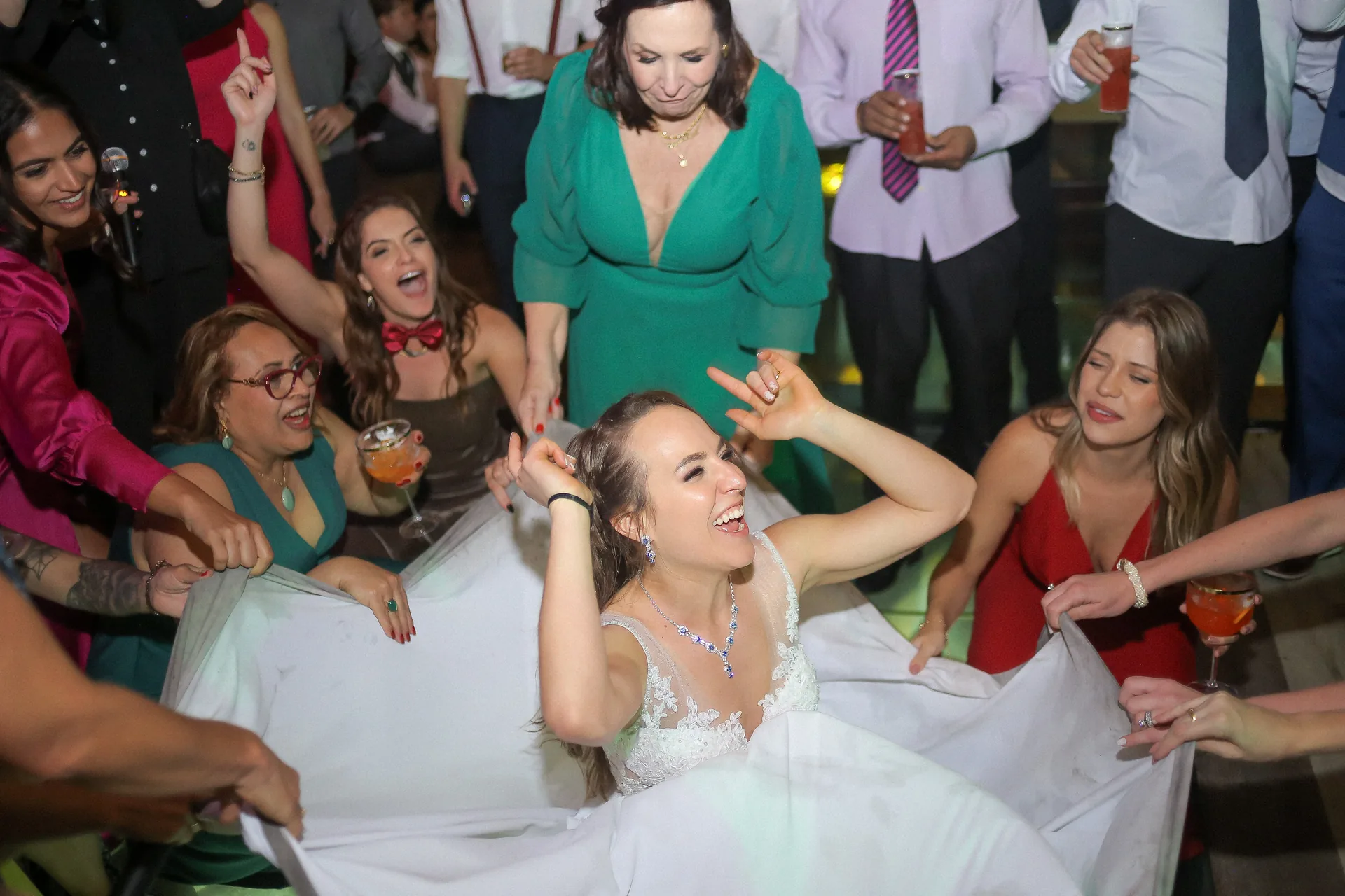 Pista de dança lotada com convidados de mãos erguidas sob luzes douradas e teto de bambu