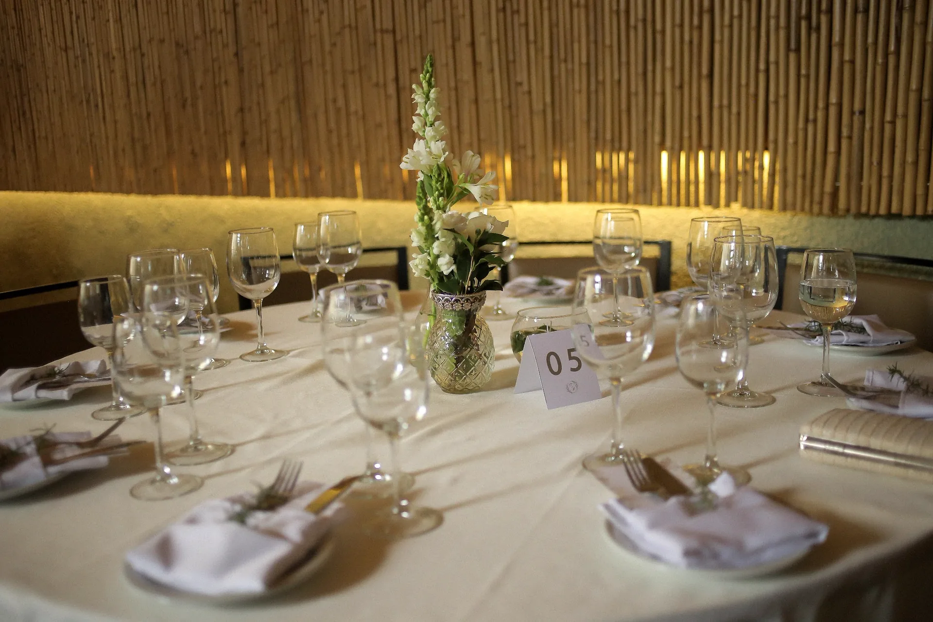 Mesa redonda posta com taças de cristal, guardanapos e flores brancas
